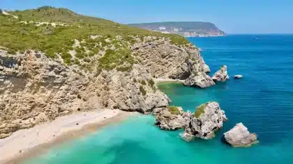 Luftaufnahme einer abgelegenen Bucht mit türkisfarbenem Wasser, feinem Sand und grünen Hängen