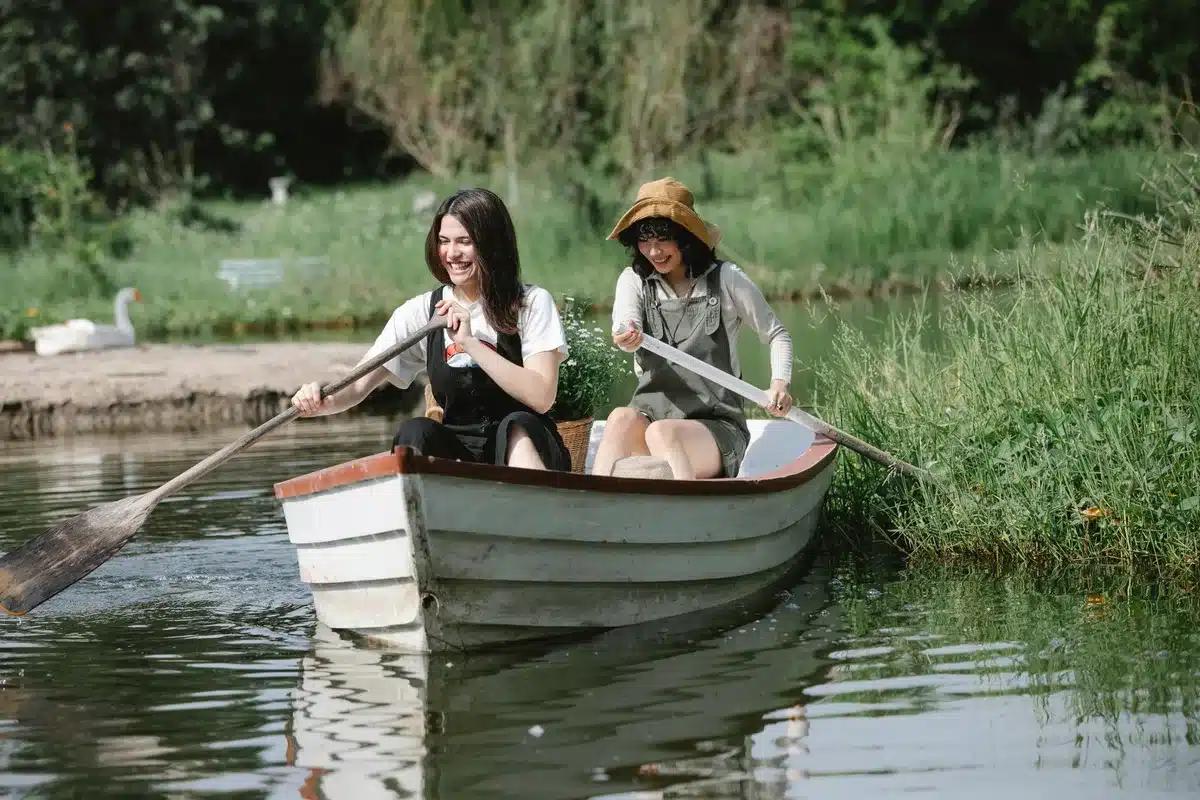 Ältere Frauen lachen zusammen auf einem Steg am See, umgeben von Natur und Booten.