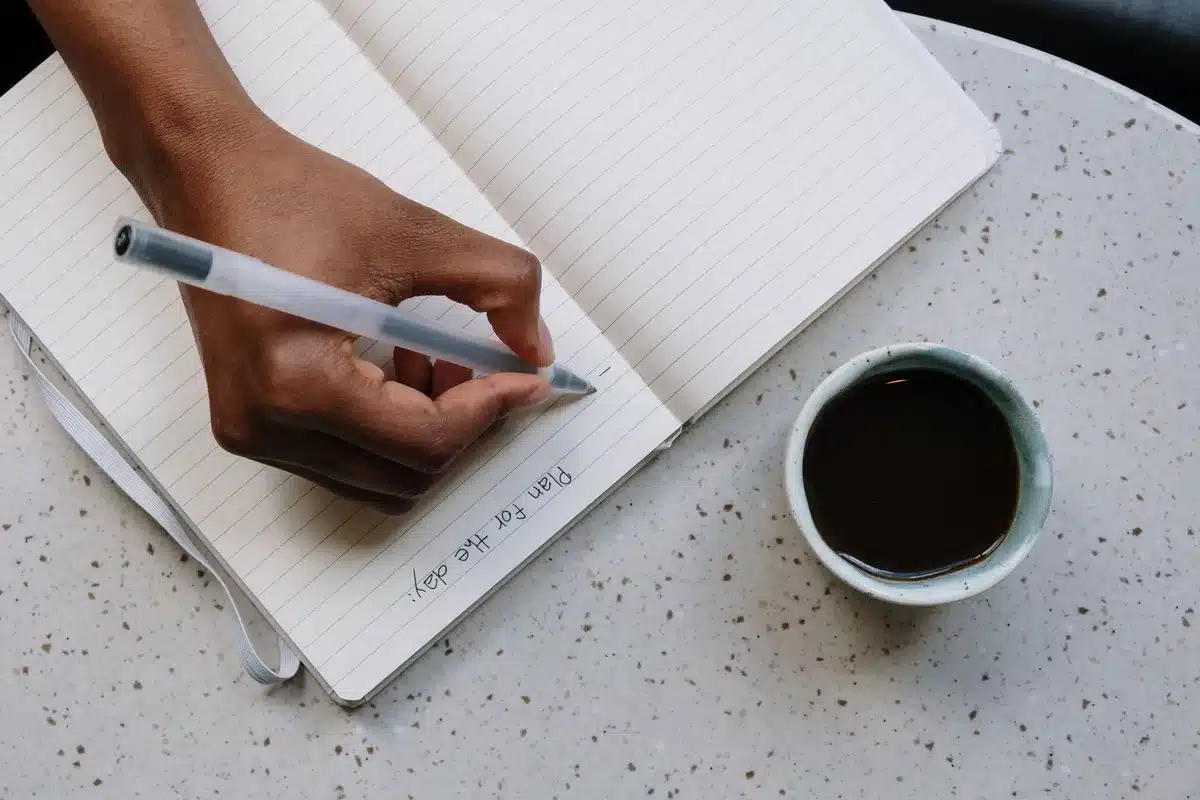 Eine Person plant ihren Tag mit Notizbuch und Kaffee am Morgen