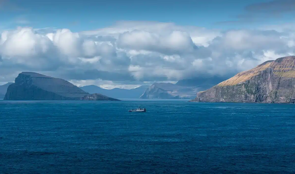 Boot vor hohen Basaltklippen der Färöer mit Seevögeln in der Luft
