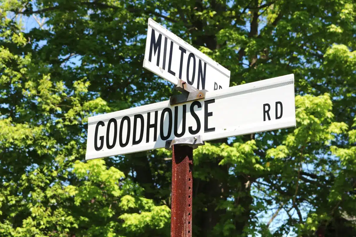 Altes Straßenschild mit kolonialer Inschrift neben einem neuen lokalen Ortsnamen.