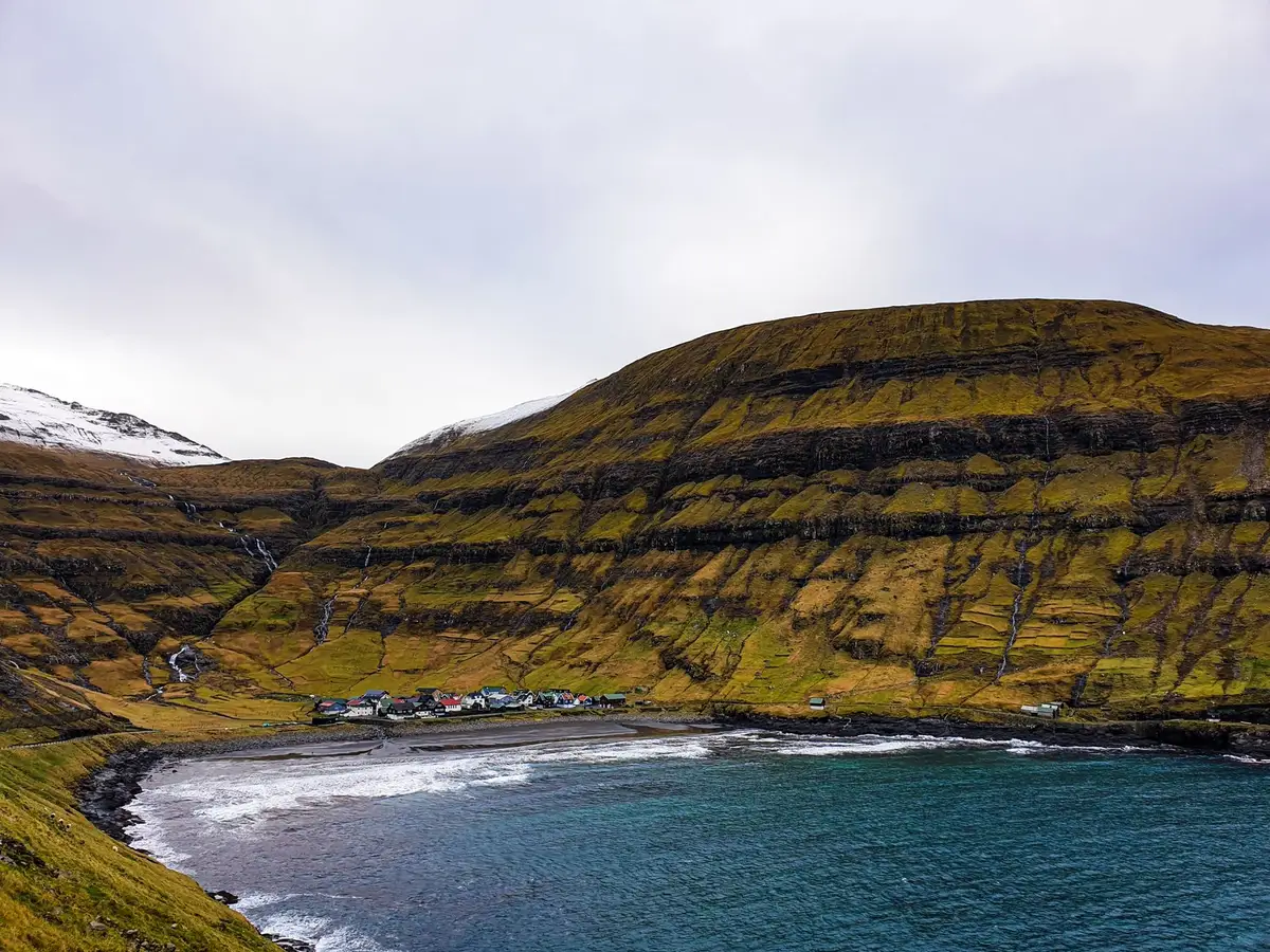 Dramatische Küstenklippen über einem kleinen Dorf mit traditionellen Häusern auf der Insel Streymoy