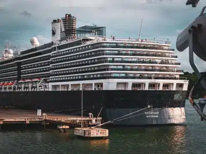 Passagiere an der Reling eines Kreuzfahrtschiffs blicken auf einen Hafen am Horizont