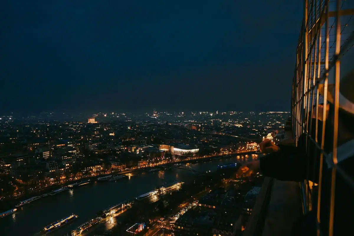 Mehrere Besucher auf einer Aussichtsplattform mit nächtlicher Skyline im Hintergrund