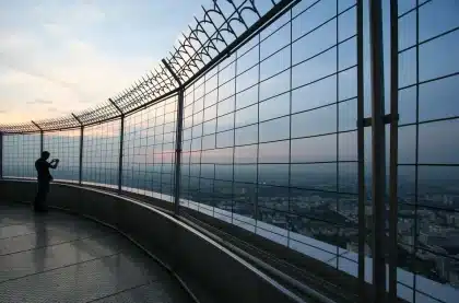 Besucher auf einer Aussichtsplattform mit Blick auf eine beleuchtete Stadtsilhouette bei Sonnenuntergang