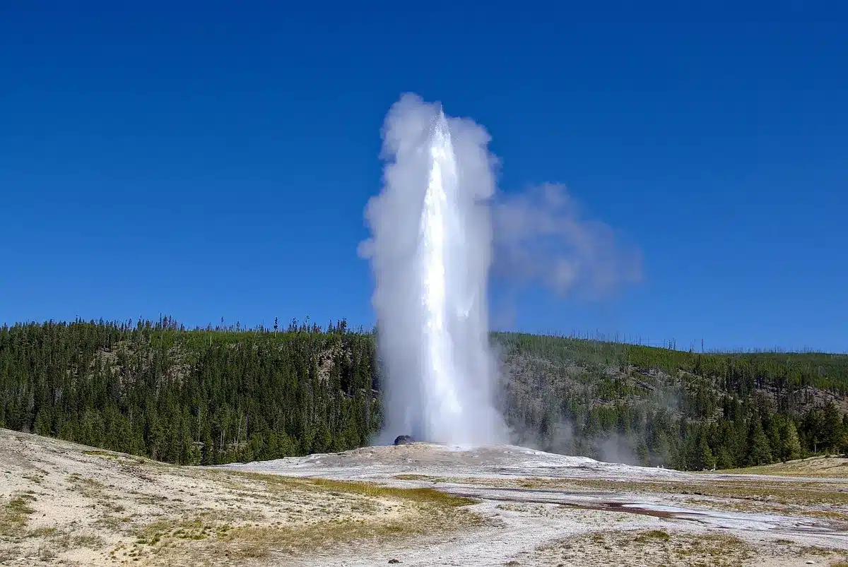 Der Geysir Old Faithful beim Ausbruch vor einer Holzlog‑Lodge