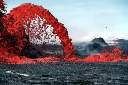 Silhouette einer Küstenlinie, dunkle Vulkanaschewolke über dem Meer und Boote im Vordergrund