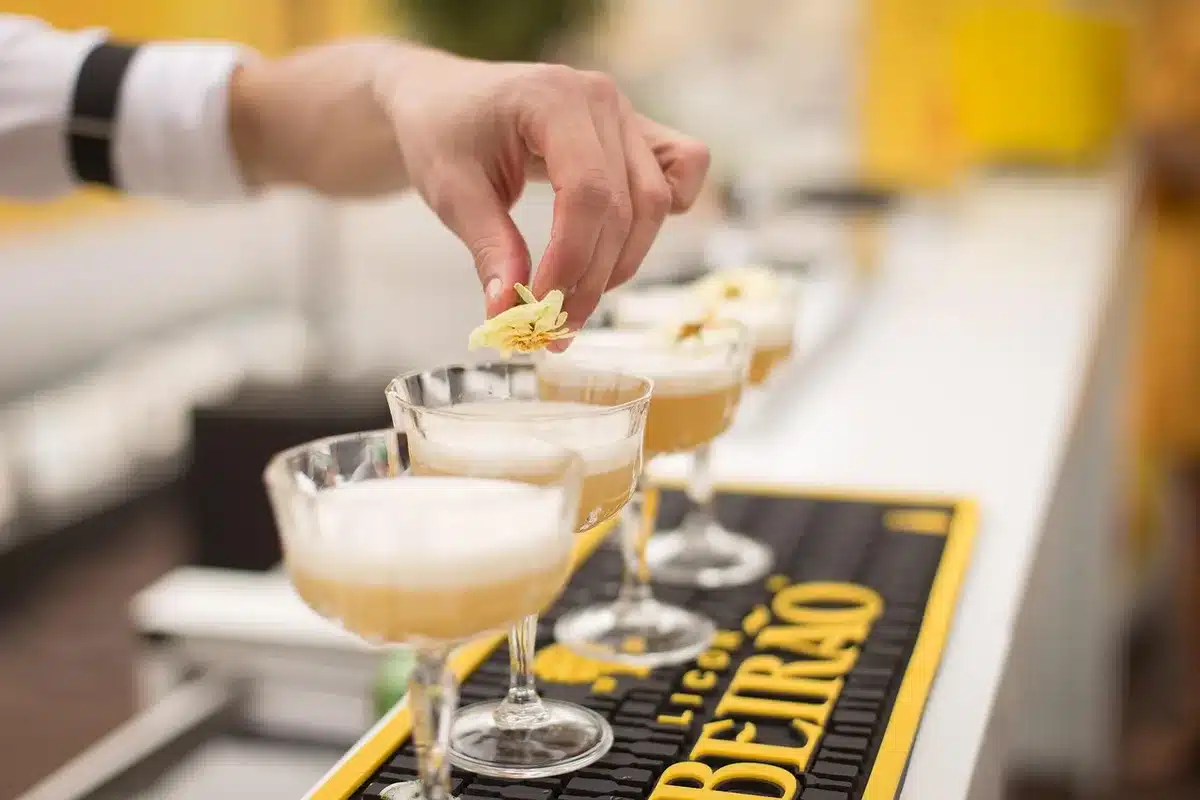 Bartender hält ein Glas mit dunklem Drink und ein kleines Einmachglas daneben