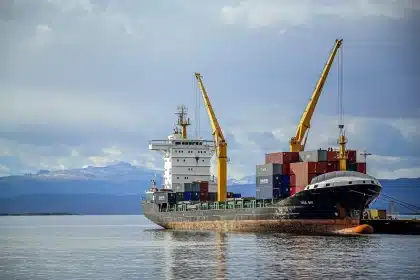 Anonymisiertes Werftdock mit Schiffsrumpf, Kransilhouette und Arbeitern in der Ferne