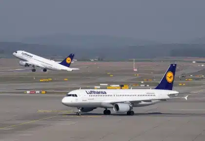 Reisender mit Rollkoffer vor einer digitalen Abflugtafel in einem modernen Flughafen