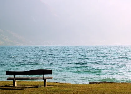 Anonymer Seeufer-Picknickplatz mit Bank, Fahrrad und weitem Wasser bei Sonnenuntergang