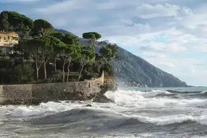Passagiere als Silhouetten auf Kreuzdeck mit Blick auf eine mediterrane Küste und Hafen